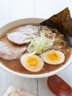 a bowl of ramen with meat, noodles and hard boiled egg on the side