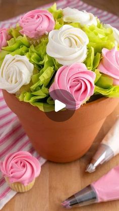 a vase filled with pink and white flowers next to cupcakes on a table