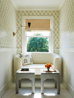 a white couch sitting under a window in a living room next to a table with flowers on it