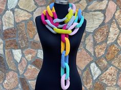 a multicolored knitted scarf on a mannequin head stand in front of a stone wall