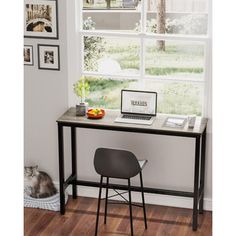 a computer desk with a laptop on it in front of a window and a cat