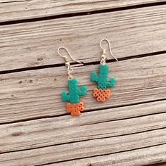 the earrings are made out of clay and have small cactus designs on them, sitting on a wooden surface