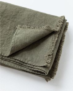 two folded linens on top of each other, one with frayed edges and the other in green