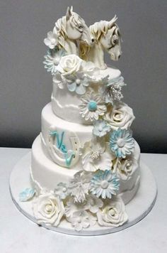 a three tiered wedding cake with white flowers and horses on top