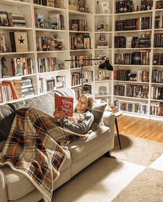 a person laying on a couch with a book in their hand and some bookshelves behind them