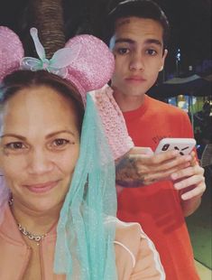 two people are posing for a photo with minnie mouse ears on their head and one is holding a cell phone