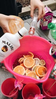 someone is pouring orange juice into a pink bucket filled with lemons and other fruit