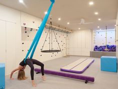 a woman doing a handstand on top of a pole in a room with climbing walls