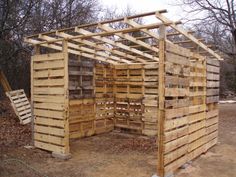 a building made out of wooden pallets in the middle of some dirt and trees