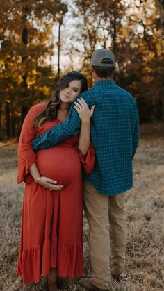 a pregnant woman hugging her husband while standing in the grass