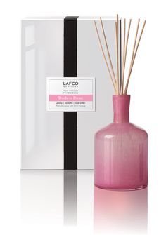 a pink vase with reeds in it next to a white and black striped box