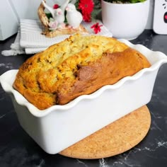 a loaf of bread sitting in a white dish on top of a counter next to a potted plant