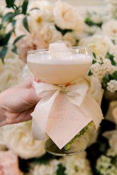 a person holding a wine glass with a card in it next to some white flowers