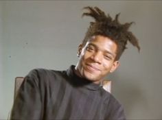 a young man with dreadlocks sitting in front of a computer monitor and smiling at the camera