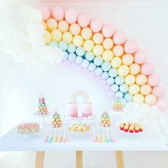 a table topped with lots of desserts and rainbow shaped balloons above the top of it