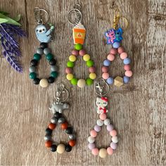 four keychains with different colored beads and charms attached to them on a wooden surface