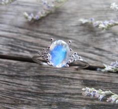 a ring with an oval shaped rainbow colored stone surrounded by small white flowers on top of a wooden surface