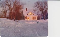 a small white house sitting on top of a snow covered hill in front of trees