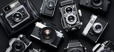 many old cameras are arranged together on a black surface with one camera facing the viewer