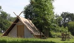 a teepee hut in the middle of a field with trees and grass around it