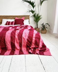 a bed covered in pink and white sheets next to a potted plant on top of a wooden headboard