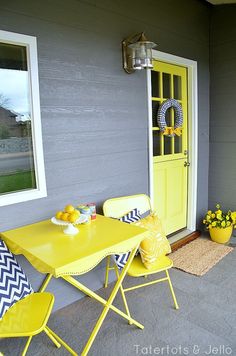 a yellow table and chairs on a porch next to a yellow door with blue and white pillows