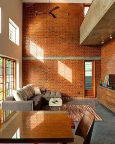 a living room filled with furniture next to a tall brick wall covered in windows and a ceiling fan