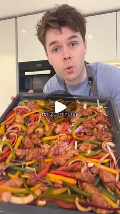 a man holding a pan full of chicken and peppers in the middle of his face