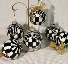 four black and white christmas ornaments on a stand with gold ribbon hanging from the top