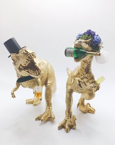 two gold dinosaur figurines with hats and glasses on their heads, one holding a beer