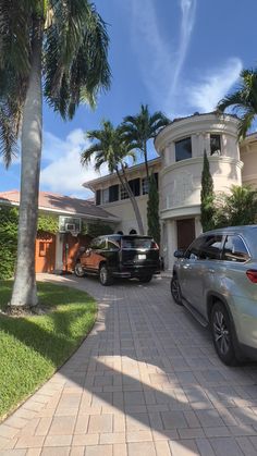 two cars parked in front of a house with palm trees on the side of the road