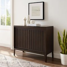 a wooden cabinet sitting on top of a hard wood floor next to a potted plant