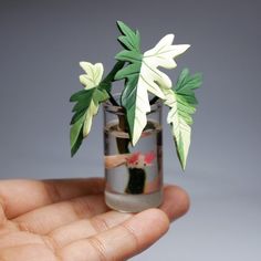 a hand holding a small glass vase filled with flowers and leaves on top of it