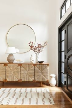 a living room with a rug, mirror and vases on the sideboard in front of it