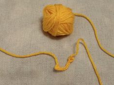 a ball of yellow yarn sitting on top of a white cloth next to a knitting needle