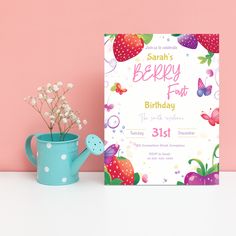 a pink and blue watering can next to a birthday card on a table with flowers