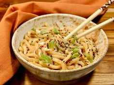 two chopsticks in a bowl of noodles with sesame seeds and scallions