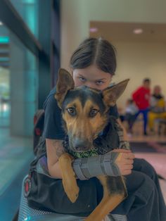 a woman holding a dog in her arms while sitting on a luggage bag at an airport