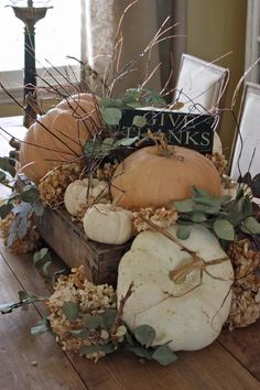 a wooden box filled with lots of pumpkins and greenery on top of a table