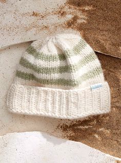 a white and green knitted hat laying on top of a pile of brown dirt