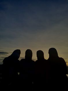 three people are sitting on a bench watching the sun go down in the sky above them