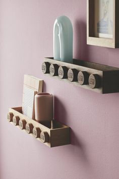 two wooden shelfs with magnets and cups on them against a pink painted wall