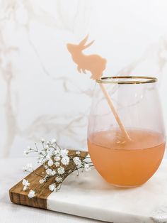 a glass filled with liquid sitting on top of a wooden cutting board next to flowers