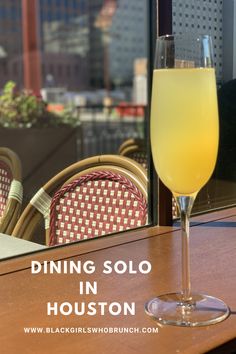 a glass filled with yellow liquid sitting on top of a table next to a window