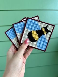 a hand holding two small cross stitch coasters