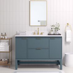 a bathroom with a blue vanity and white tile walls, along with gold accents on the mirror