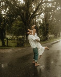 a man and woman dancing in the rain on a rainy day with trees behind them