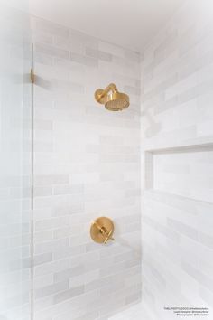 a white tiled shower with gold faucet and hand held shower head in the corner