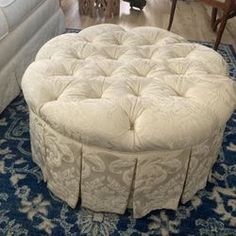 a round ottoman sitting on top of a blue rug in front of a white couch