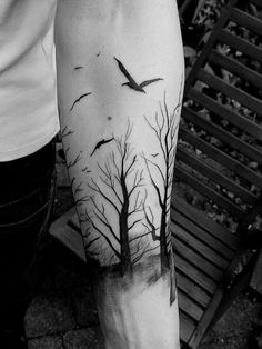 a person with a tree and birds tattoo on their arm, next to a bench